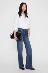 Modell iført Anine Bing Hugh Jean 34" i dark indigo med knappegylfet og wide leg-passform, stylet med hvit skjorte, sort skinnveske og sorte spisse flate sko
